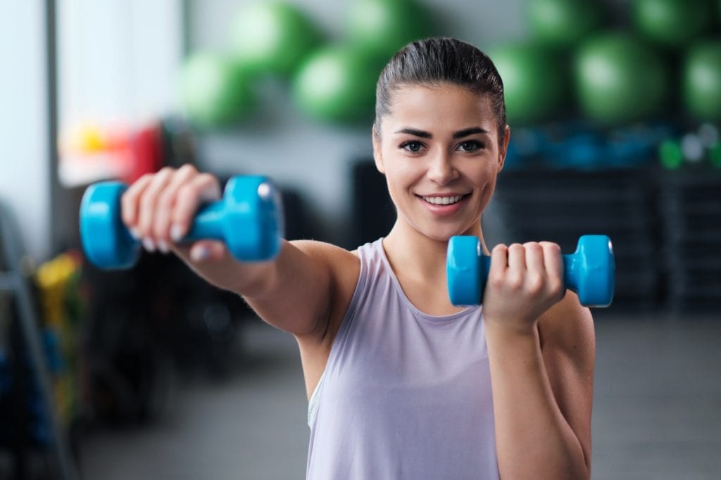 A beautiful athletic young brunette woman in sportswear trains in the gym. Copy Space.